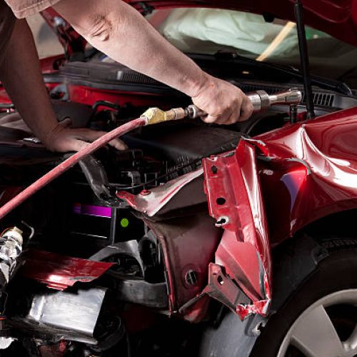 Closeup photo of an auto body mechanic using a compressed air wrench to remove the side fender from a vehicle that was in an auto accident.